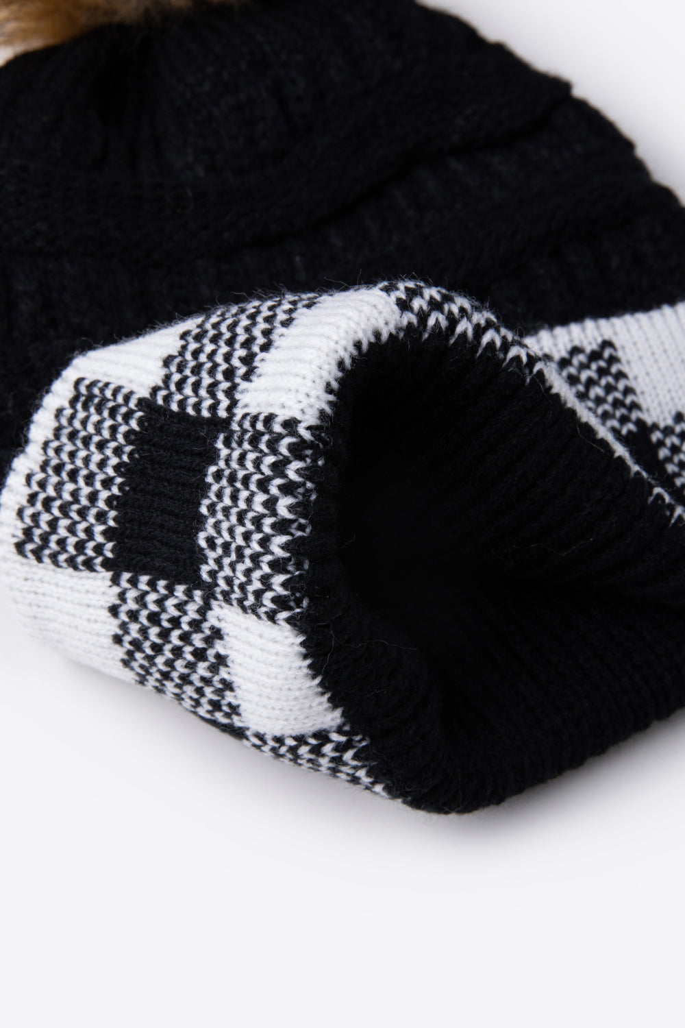 A stylish plaid pom-pom knit beanie in a flat lay style, showcasing its soft acrylic material and trendy design.