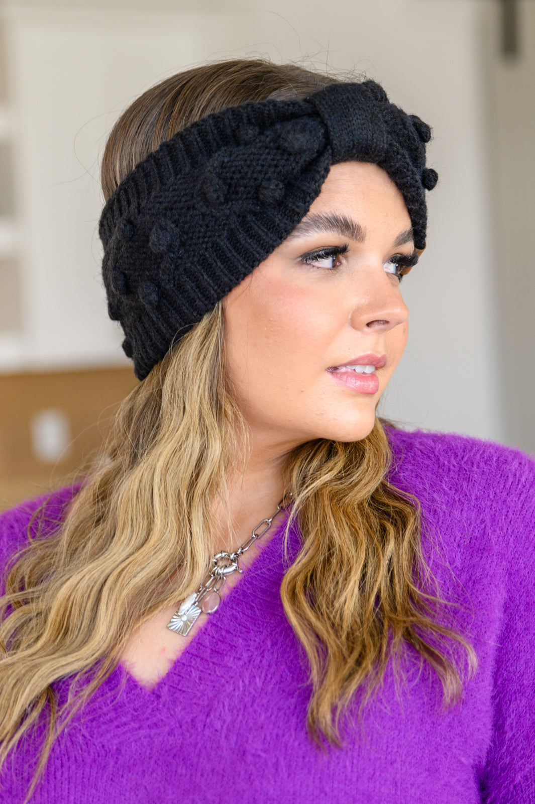 Black Pom Knit Headwrap featuring a bow front and pom pom detailing, made from soft ribbed knit material.