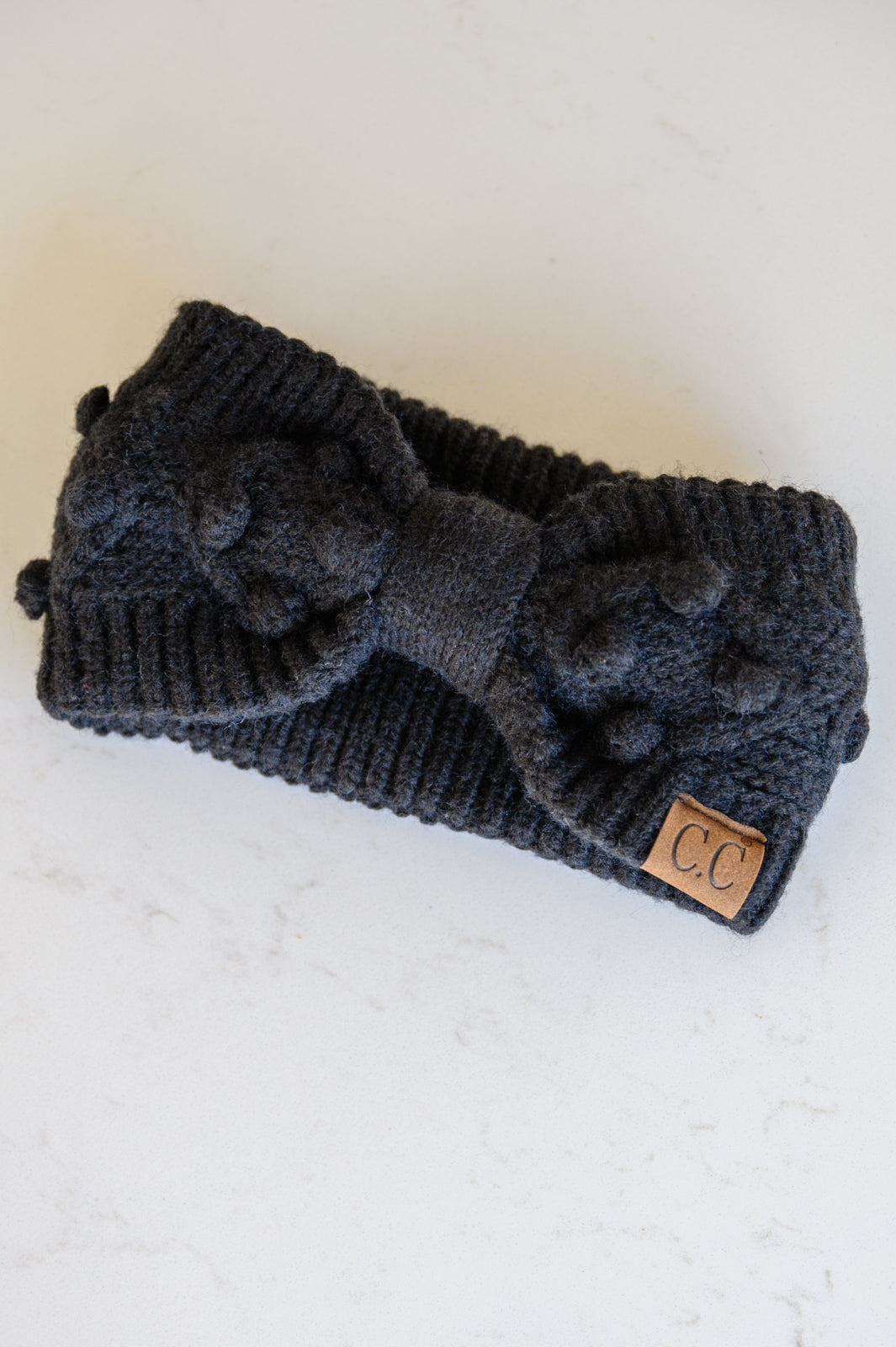 Black Pom Knit Headwrap featuring a bow front and pom pom detailing, made from soft ribbed knit material.