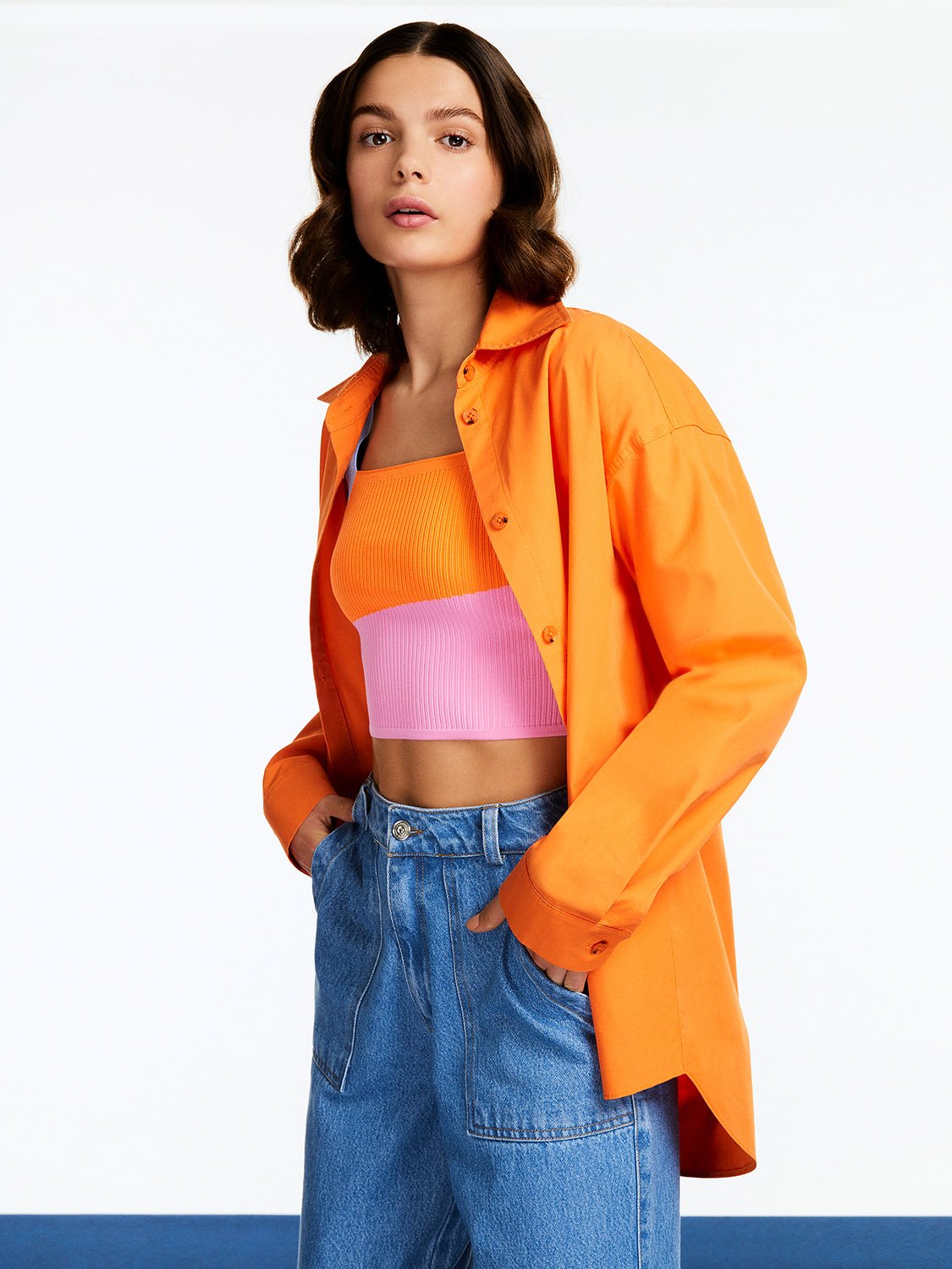 A vibrant Printed Oversized Shirt featuring orange, pink, and blue colors with long sleeves and a printed text detail on the back.