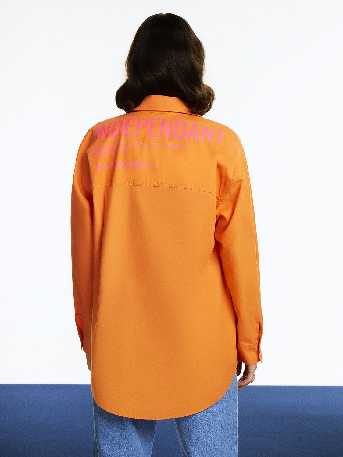 A vibrant Printed Oversized Shirt featuring orange, pink, and blue colors with long sleeves and a printed text detail on the back.