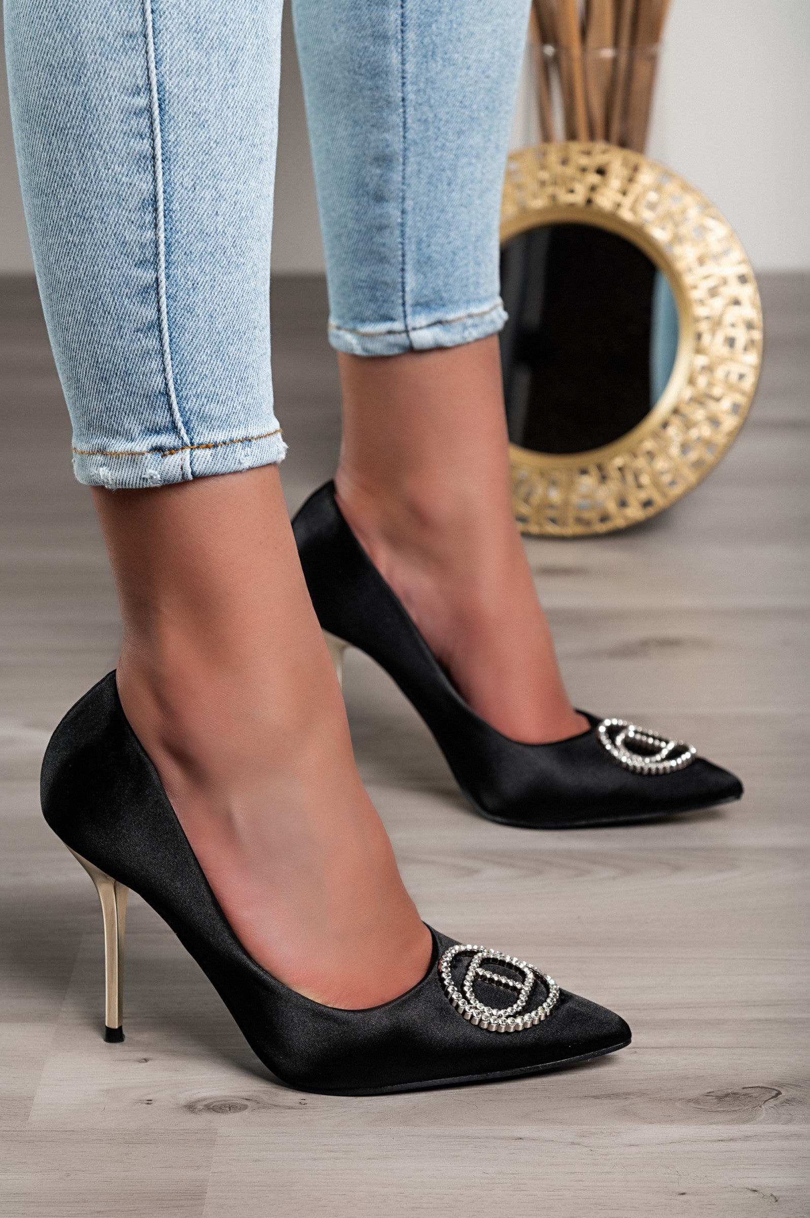 Elegant black high-heeled pumps with a decorative brooch, showcasing a pointed toe and thin heel.