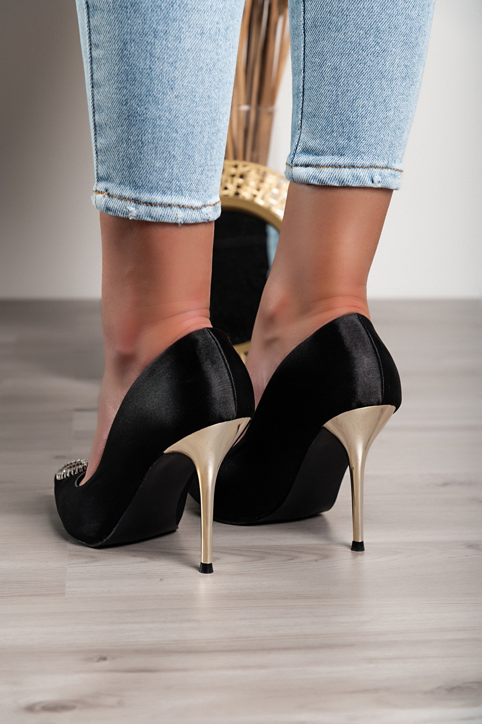 Elegant black high-heeled pumps with a decorative brooch, showcasing a pointed toe and thin heel.