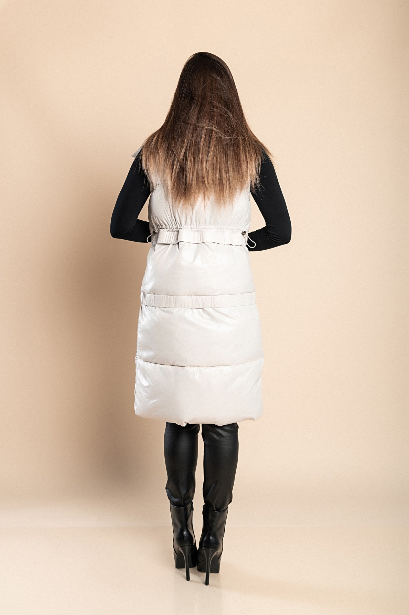 Beige quilted vest with snap buttons and buckle details, featuring a high neck and adjustable length.