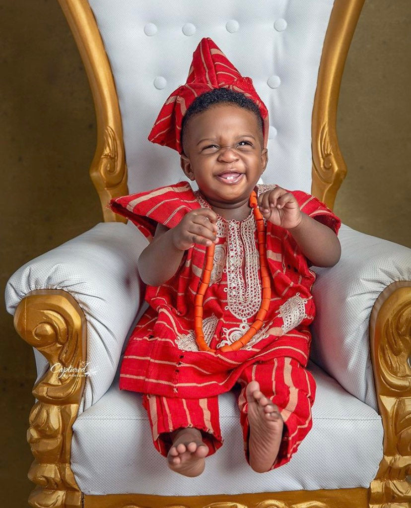 A young boy dressed in a vibrant red asooke outfit, showcasing traditional African attire with intricate patterns.