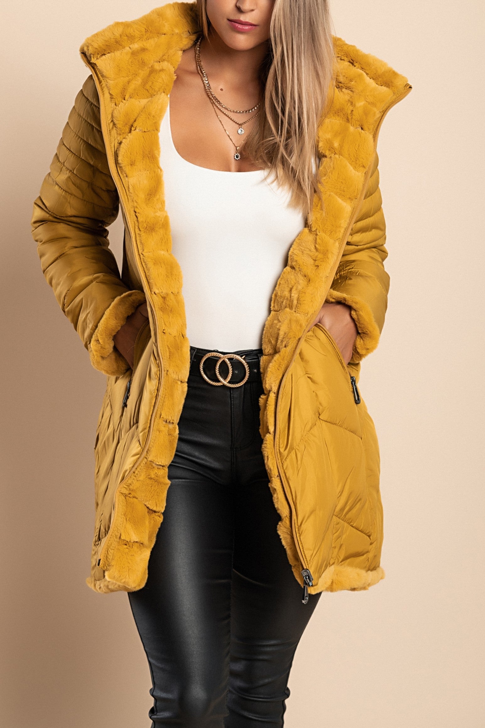 Reversible quilted jacket in mustard color with high collar and hood, featuring padded detail on one side and synthetic leather on the other.