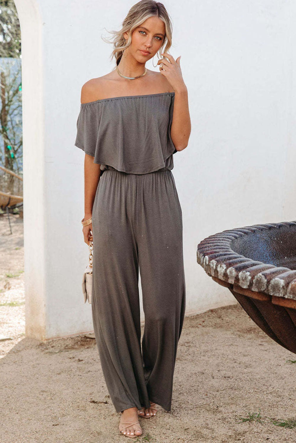 A stylish gray ruffle jumpsuit featuring an elastic frill around the shoulders and long, loose-fitting pants, perfect for casual or dressy occasions.