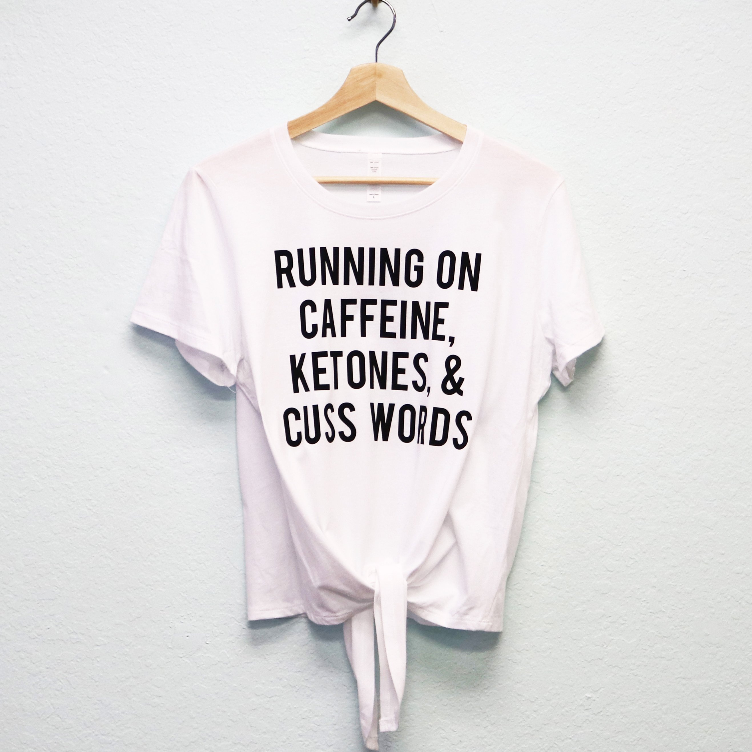 Black and white crop top with front tie featuring the slogan 'RUNNING ON CAFFEINE KETONES & CUSS WORDS'.