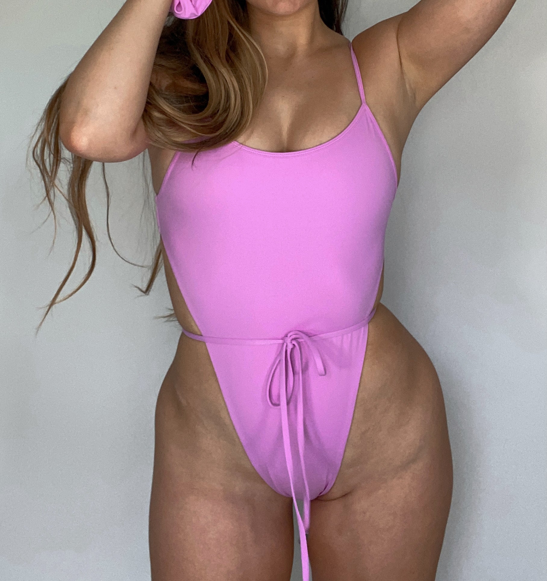 The Samira One Piece in Lilac, a sexy swimsuit with a front tie bow detail, designed to accentuate curves and made from recycled materials.