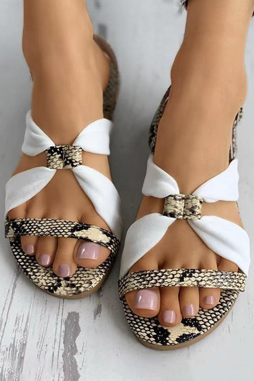 Stylish Izza white sandals with flat sole, featuring leopard pattern and crossed straps.