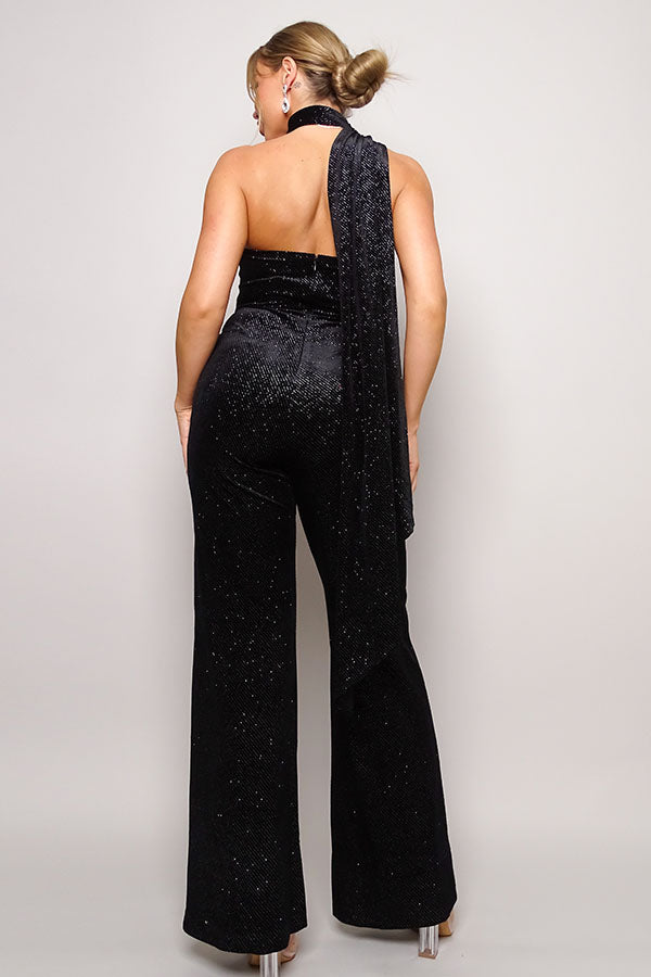 A stylish black scarf top glitter velvet jumpsuit featuring a one-shoulder design, wrap-around scarf detail, and long pants.