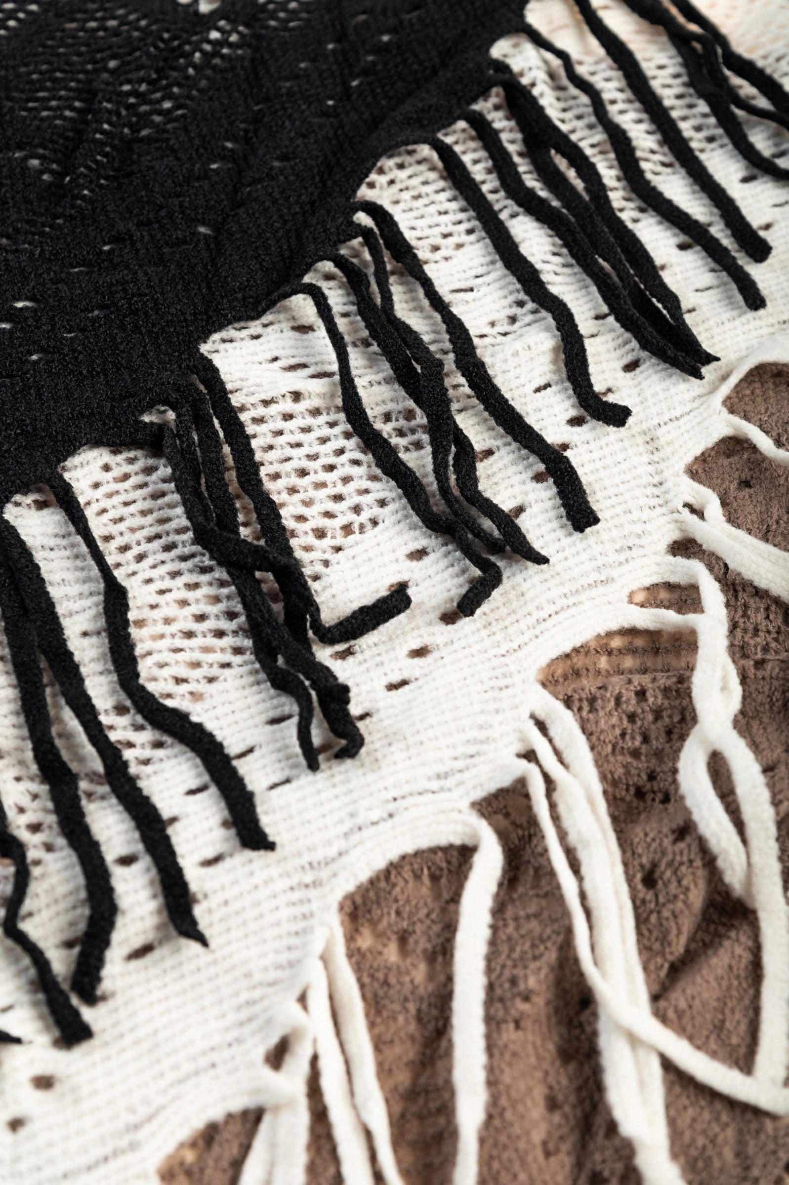 Set of 3 knitted scarves in white, black, and beige with fringes, showcasing their triangular shape and soft texture.