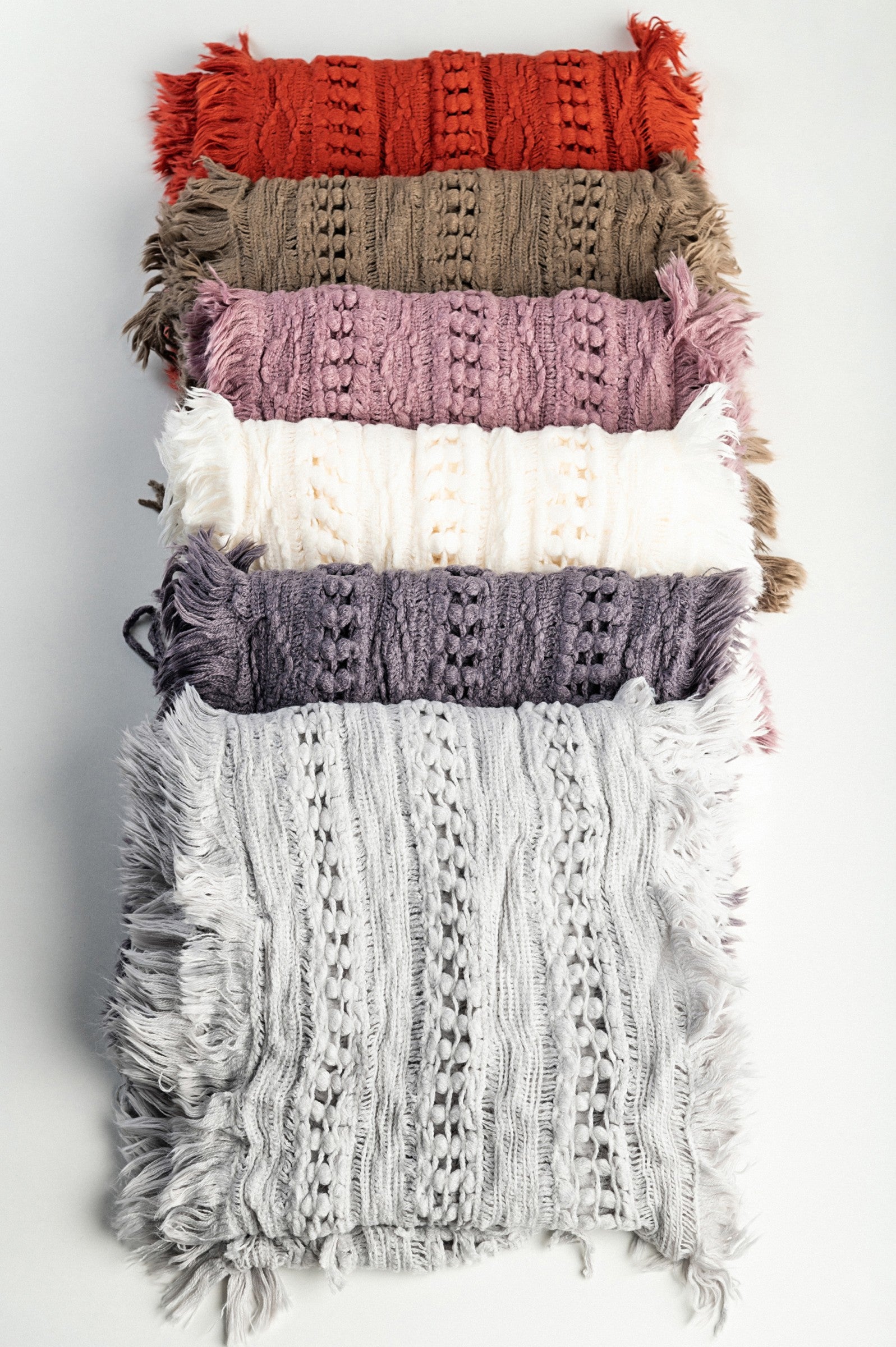 A vibrant set of six knitted scarves in white, light gray, brown, brick, pink, and purple, featuring stylish fringes.