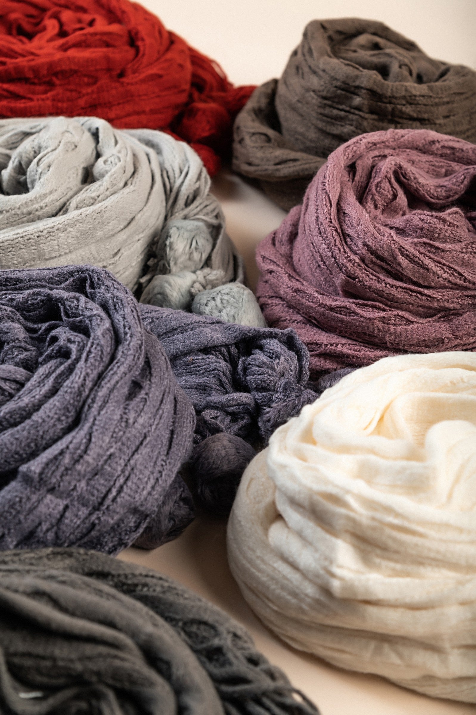 A colorful set of 7 knitted scarves in various shades including white, dark gray, purple, pink, brown, and brick, showcasing their soft texture.