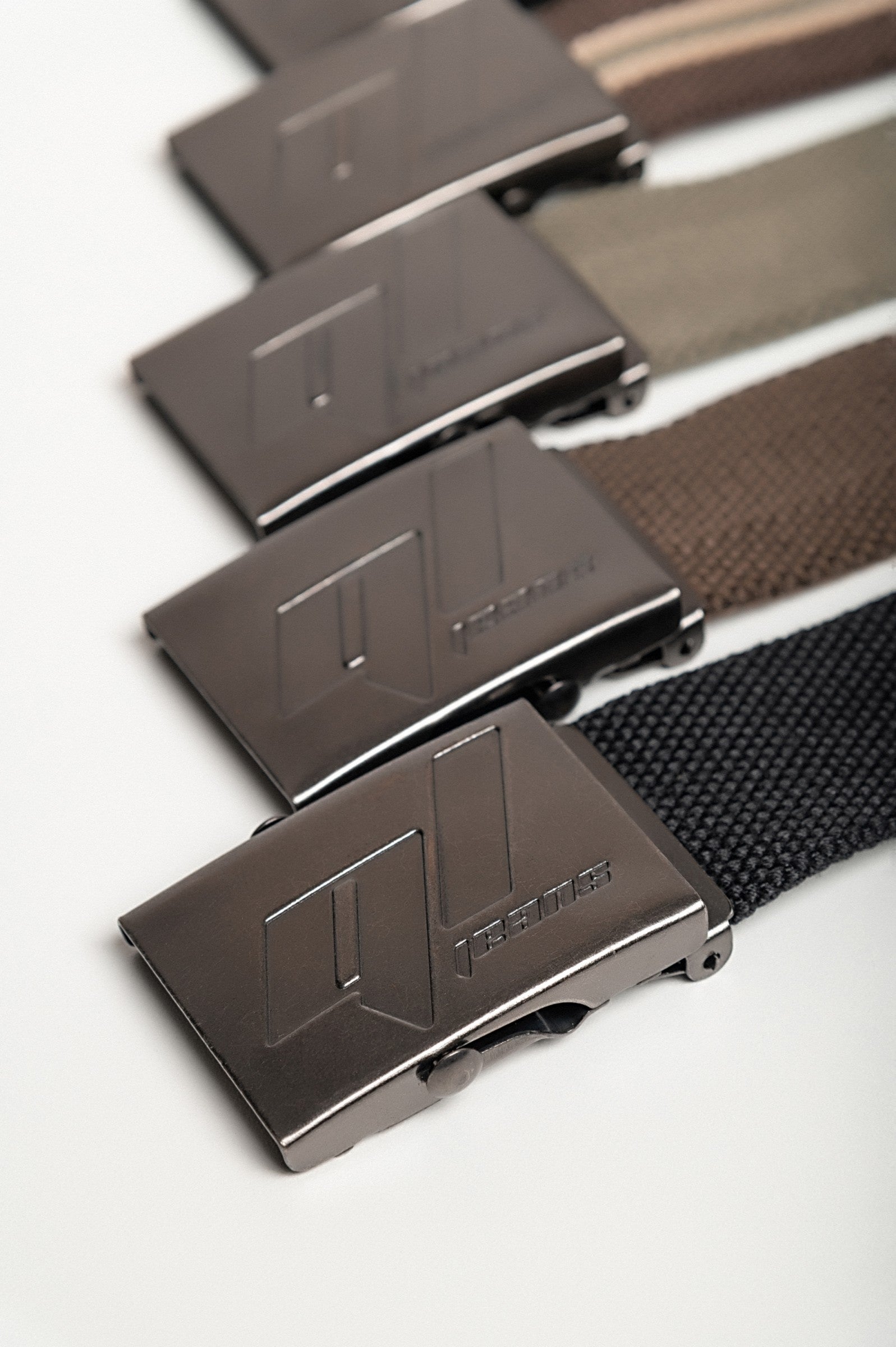 Set of five stylish belts in various colors including green, black, olive, brown, and striped, featuring a metal buckle with engraving.