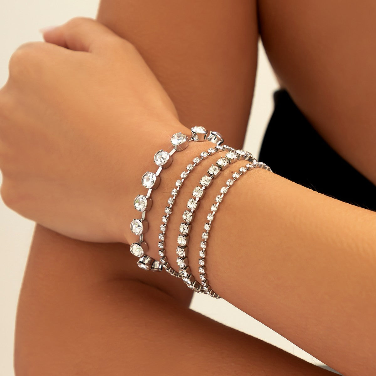 A stylish set of four white rhinestone bracelets featuring decorative stones and a metal lobster clasp, elegantly displayed.