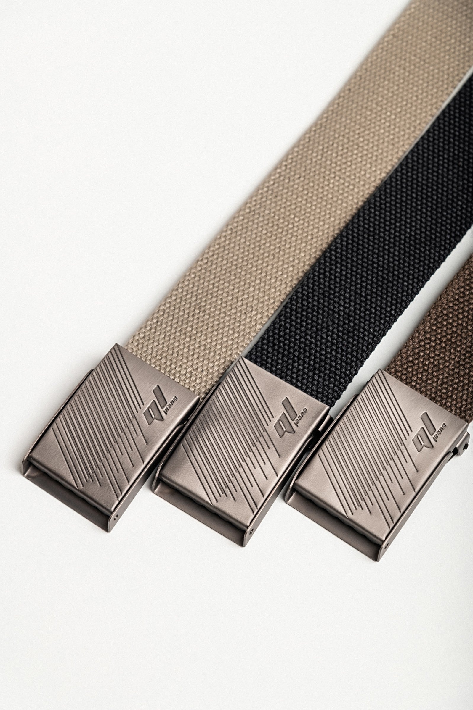 Set of three stylish belts in beige, black, and brown with metal buckles and engravings.