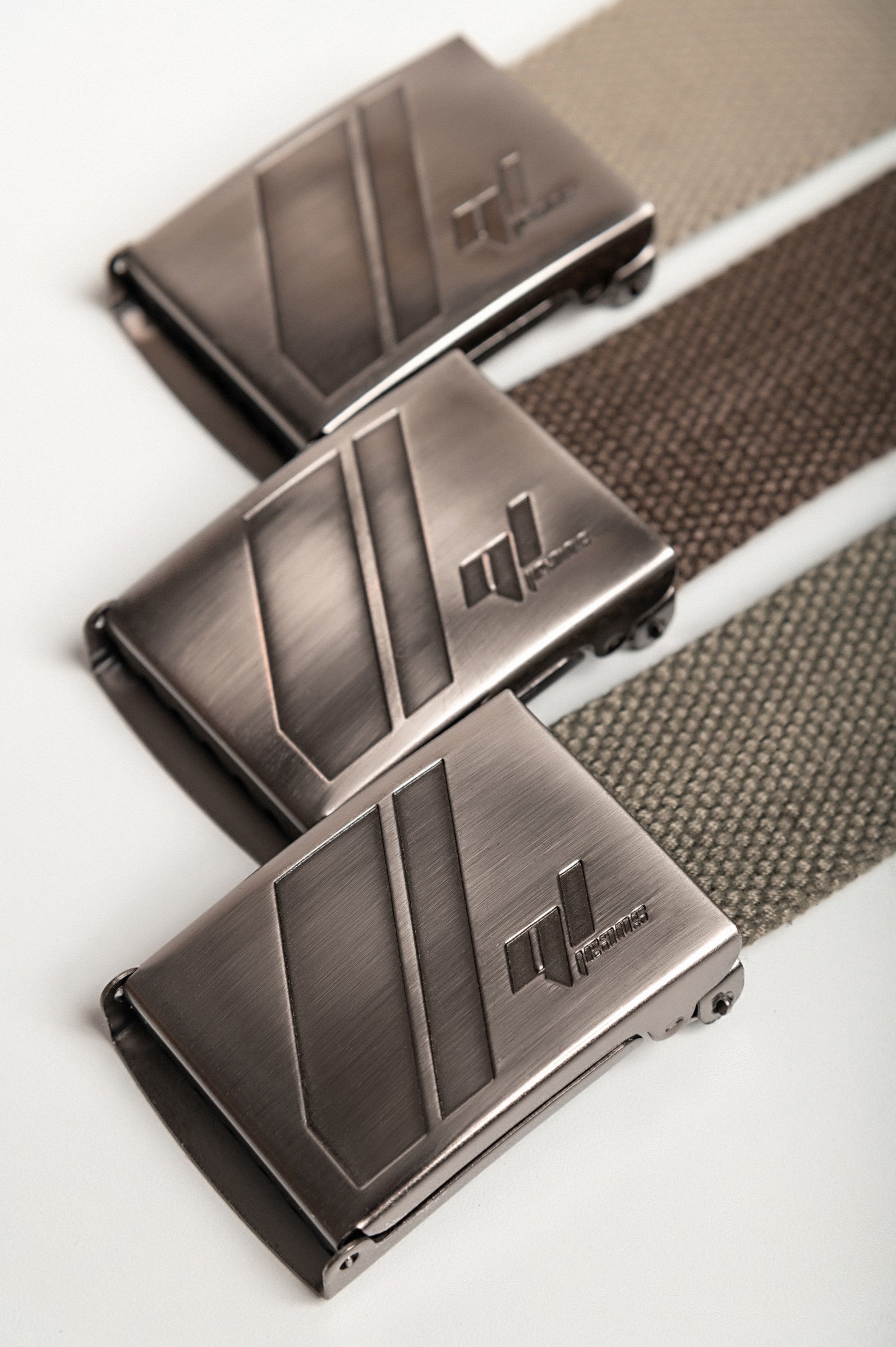 Set of three stylish belts in beige, olive, and brown with metal buckles featuring elegant engravings.