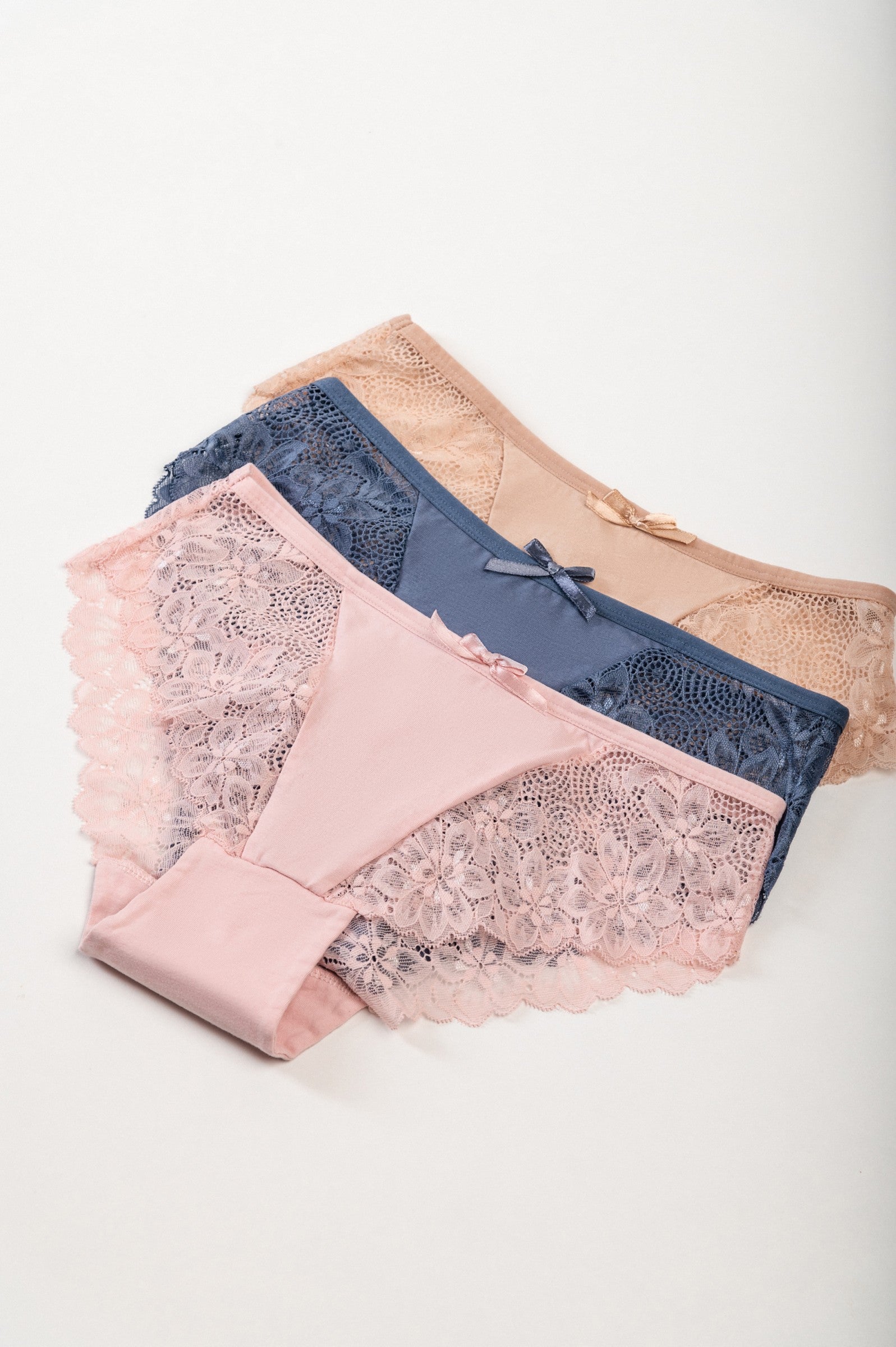 Set of three lace panties in blue, pink, and beige, showcasing their delicate design and high-quality fabric.