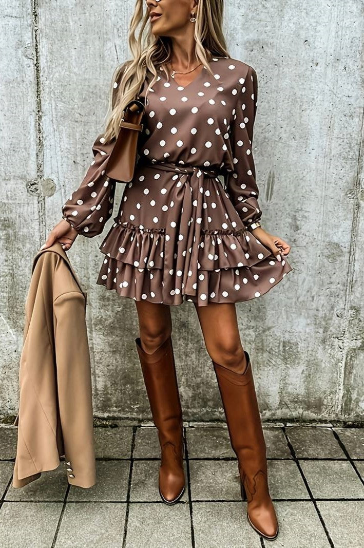 Brown mini dress with polka dot print, featuring a V-neckline, long sleeves, and a ruffled skirt, styled with a decorative belt.