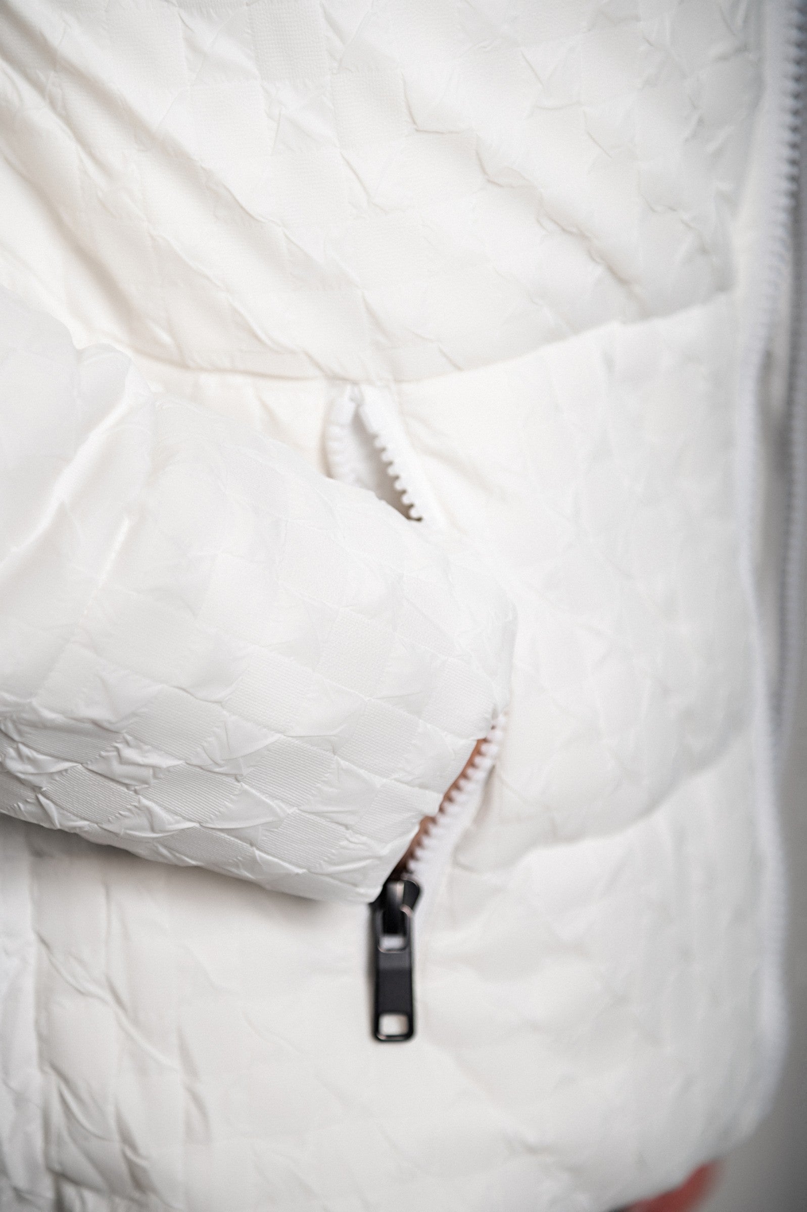 White short padded jacket with hood, featuring a high collar and zipped side pockets, perfect for winter wear.