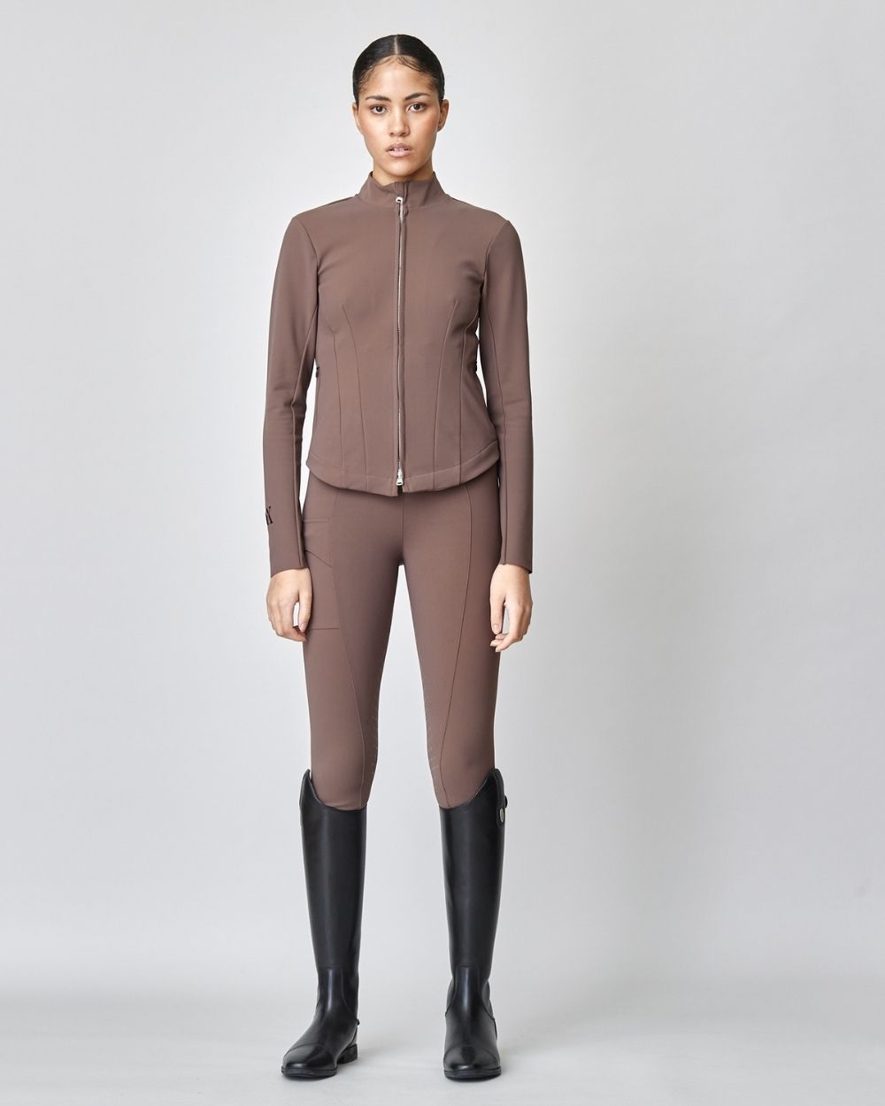 A stylish brown riding jacket made from Italian jersey fiber, featuring a fitted silhouette and laser-cut edges, perfect for equestrian activities.