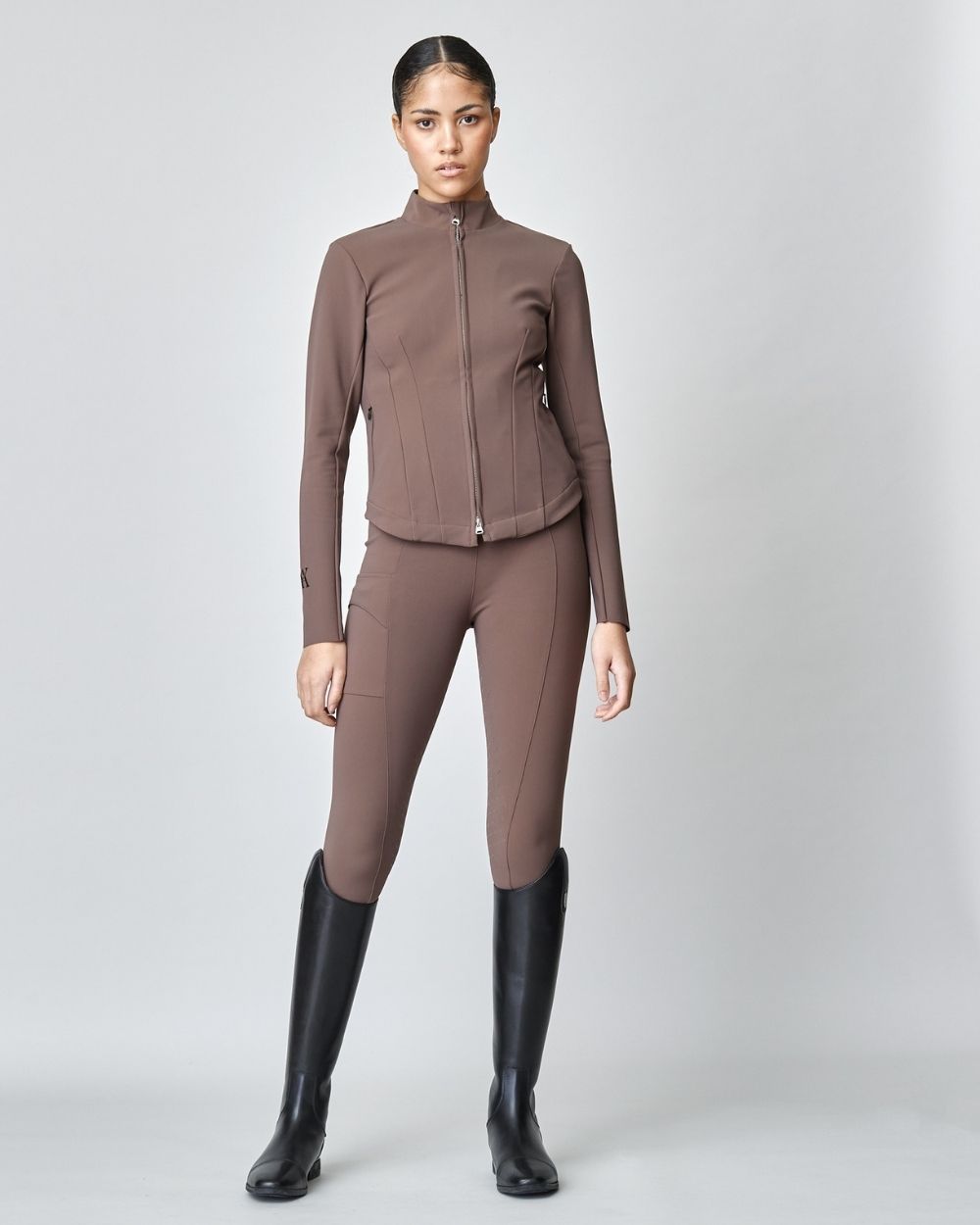 A stylish brown riding jacket made from Italian jersey fiber, featuring a fitted silhouette and laser-cut edges, perfect for equestrian activities.