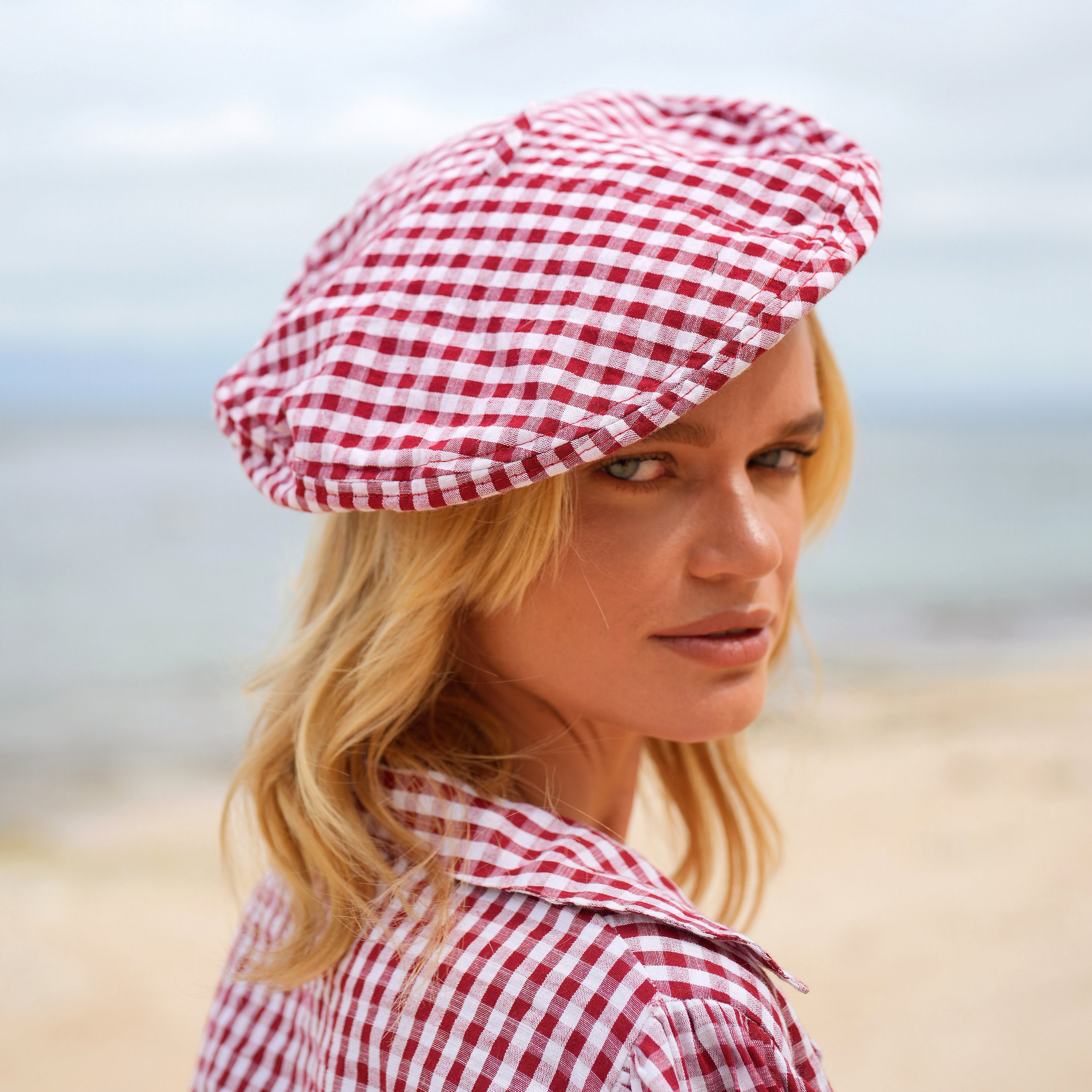 A stylish red gingham beret hat made from soft cotton with a comfortable linen lining, showcasing its eco-friendly design.