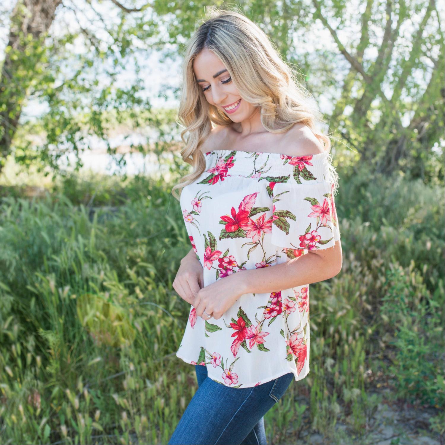 A stylish woman wearing a Smocked Floral Print Off Shoulder Top, showcasing its vibrant floral design and off-shoulder neckline.