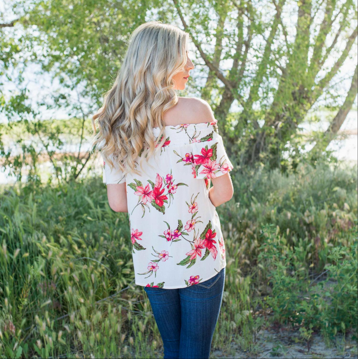 A stylish woman wearing a Smocked Floral Print Off Shoulder Top, showcasing its vibrant floral design and off-shoulder neckline.