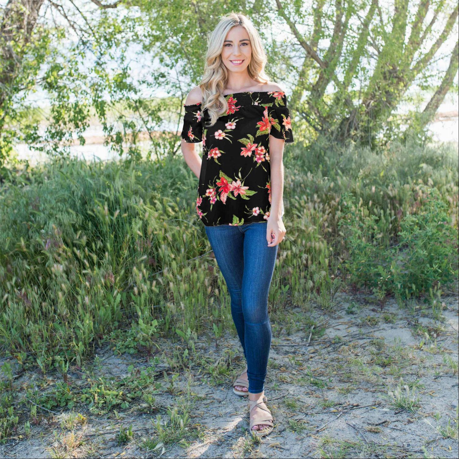 A stylish woman wearing a Smocked Floral Print Off Shoulder Top, showcasing its vibrant floral design and off-shoulder neckline.