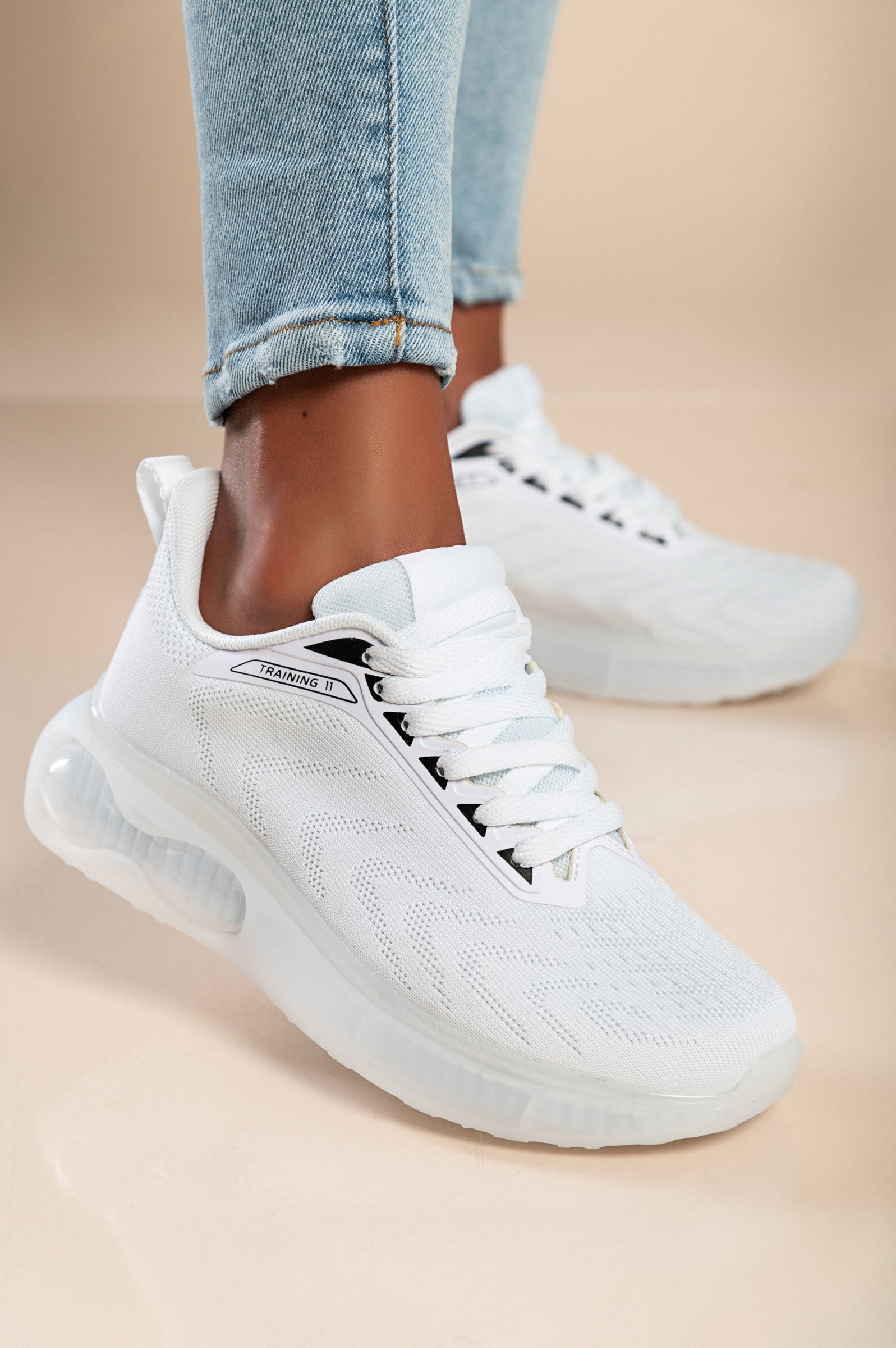 A pair of stylish white sneakers with a textile upper, round toe, and lace-up fastening, showcasing their reinforced heel and toe.