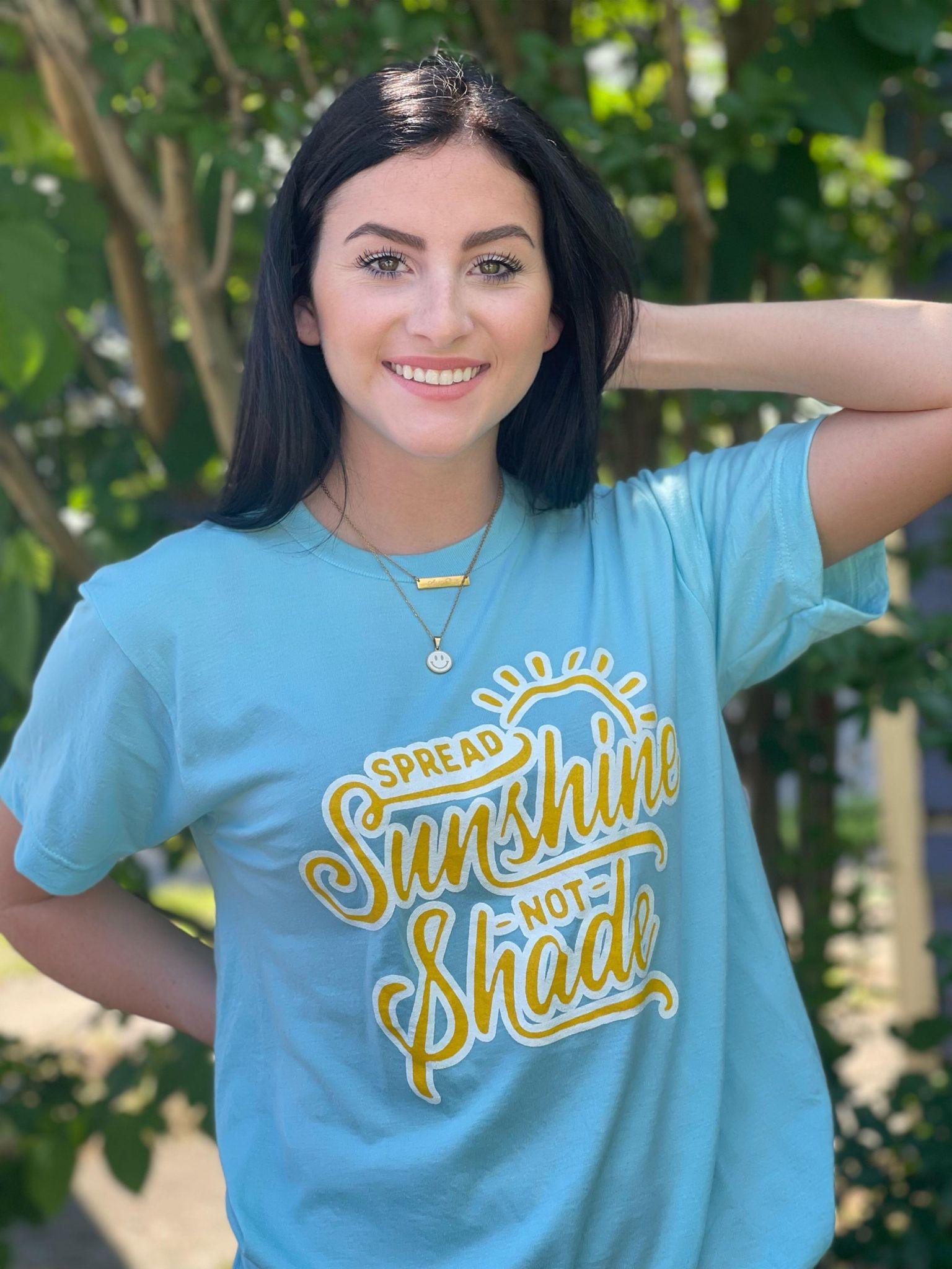 A vibrant unisex t-shirt with the phrase 'Spread Sunshine Not Shade' printed in colorful letters, showcasing a soft fabric and true-to-size fit.