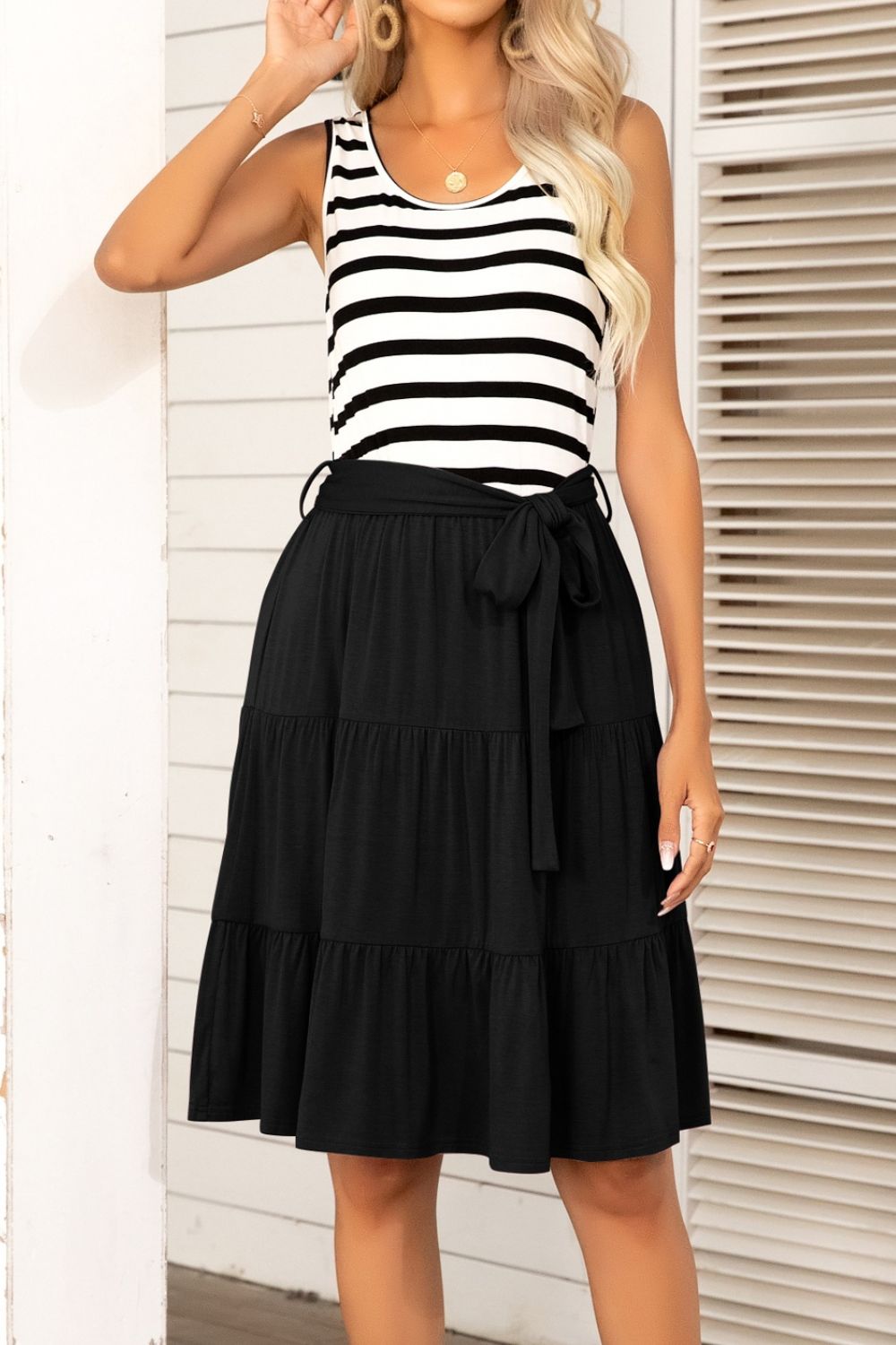 A stylish striped tie-waist sleeveless tiered dress featuring a round neckline and knee-length A-line hem, perfect for summer outings.