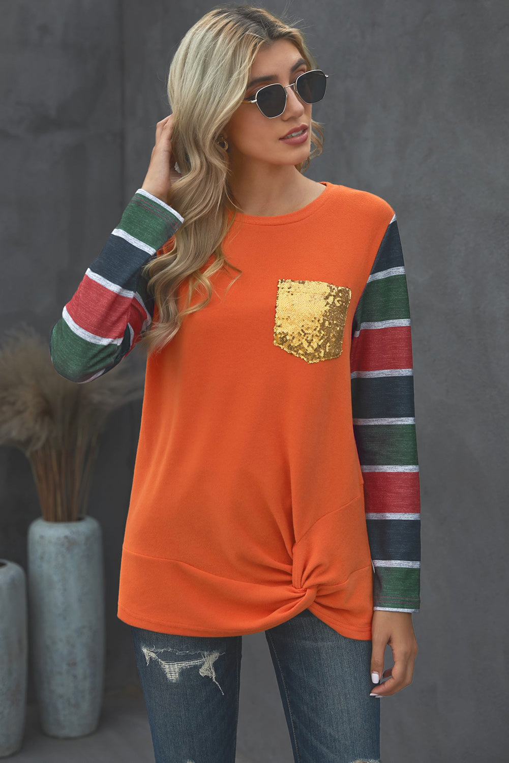 A stylish striped long sleeve top featuring a twist front design and a sparkling sequin pocket, displayed in an outdoor flat lay.