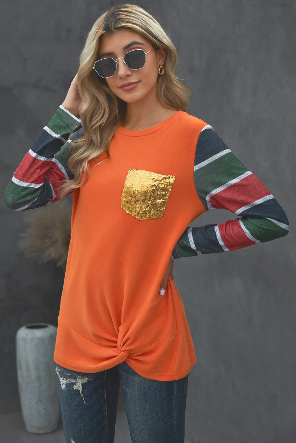 A stylish striped long sleeve top featuring a twist front design and a sparkling sequin pocket, displayed in an outdoor flat lay.