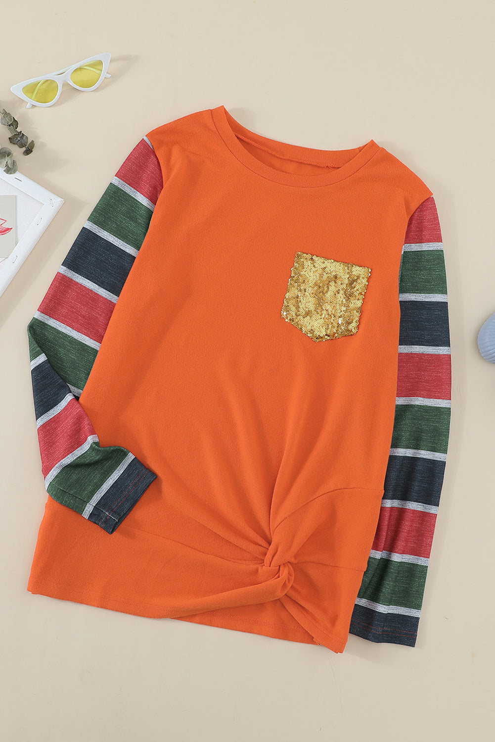 A stylish striped long sleeve top featuring a twist front design and a sparkling sequin pocket, displayed in an outdoor flat lay.