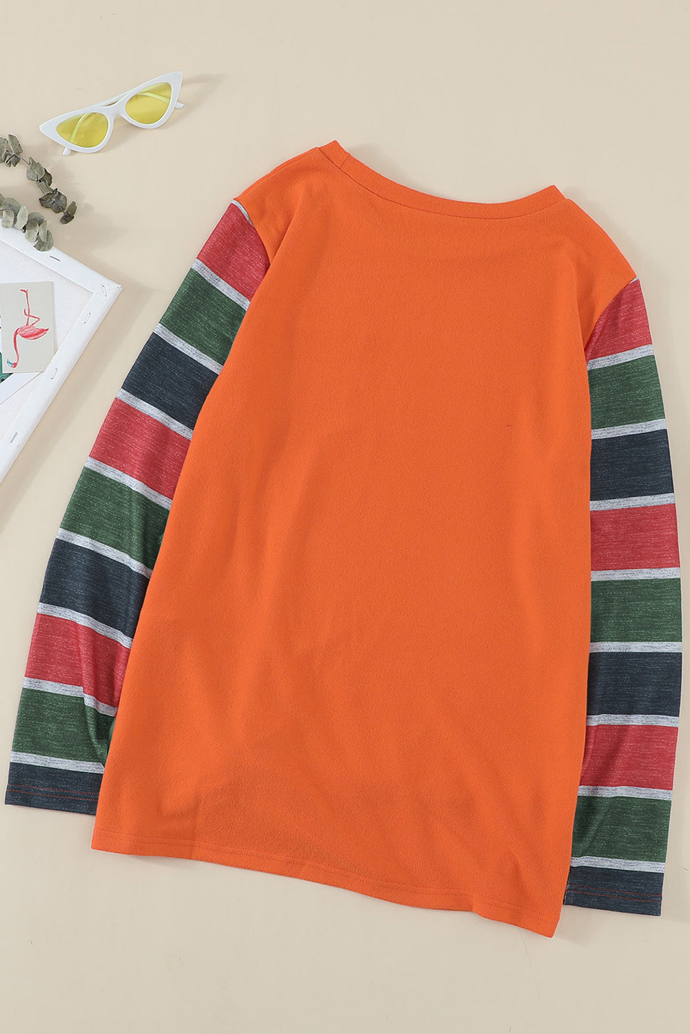 A stylish striped long sleeve top featuring a twist front design and a sparkling sequin pocket, displayed in an outdoor flat lay.