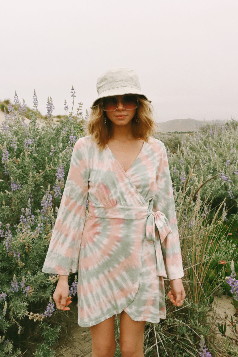 A stylish Sunrise Dress Tie-Dye featuring a saddle pink tie-dye pattern and wrap bell sleeves, perfect for any occasion.