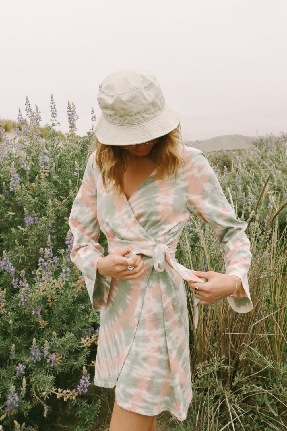 A stylish Sunrise Dress Tie-Dye featuring a saddle pink tie-dye pattern and wrap bell sleeves, perfect for any occasion.