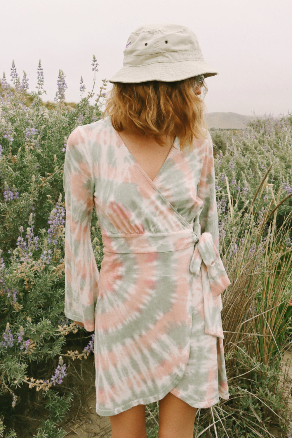 A stylish Sunrise Dress Tie-Dye featuring a saddle pink tie-dye pattern and wrap bell sleeves, perfect for any occasion.