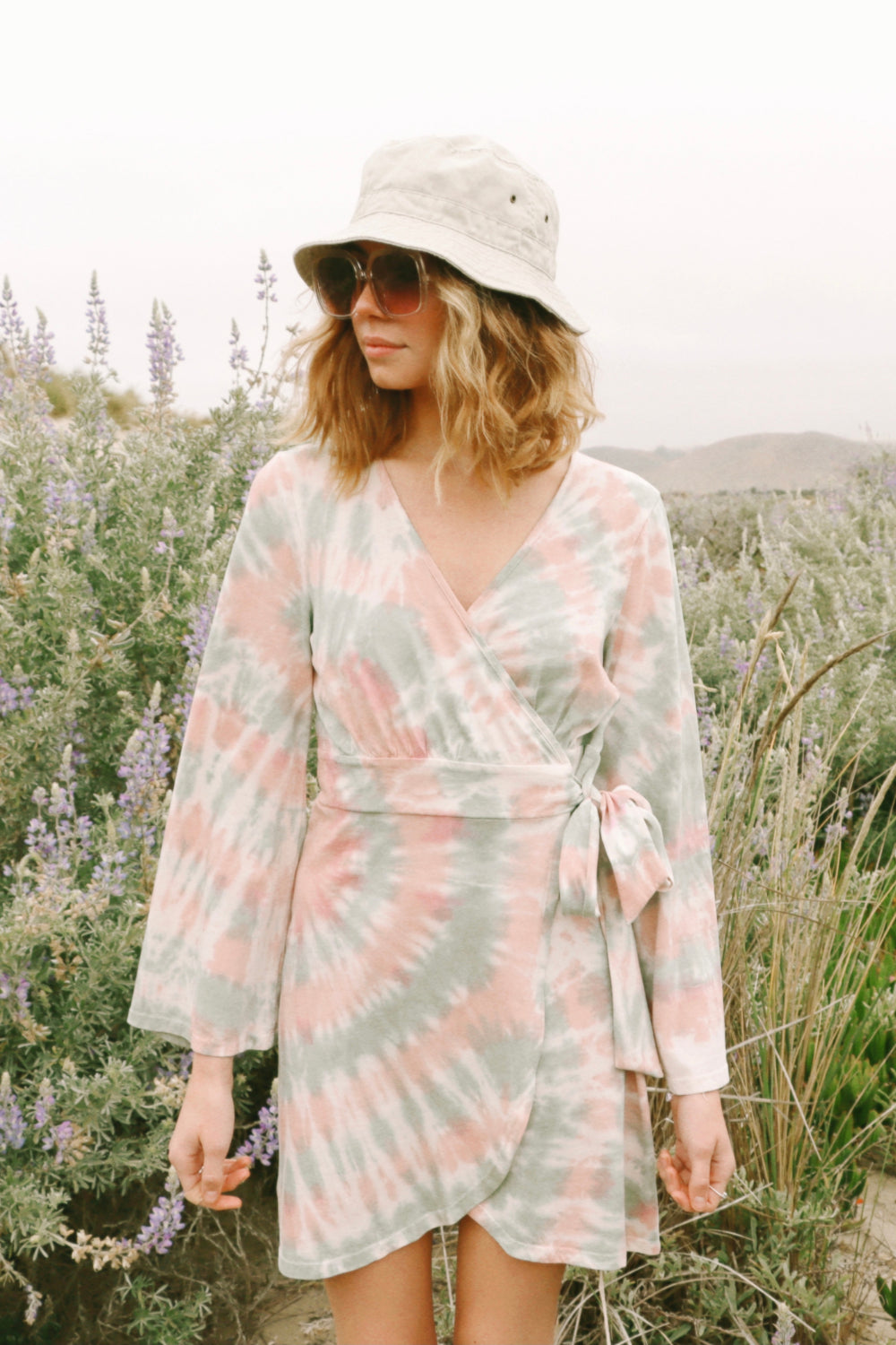 A stylish Sunrise Dress Tie-Dye featuring a saddle pink tie-dye pattern and wrap bell sleeves, perfect for any occasion.