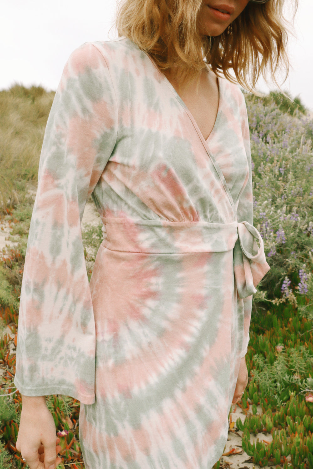 A stylish Sunrise Dress Tie-Dye featuring a saddle pink tie-dye pattern and wrap bell sleeves, perfect for any occasion.