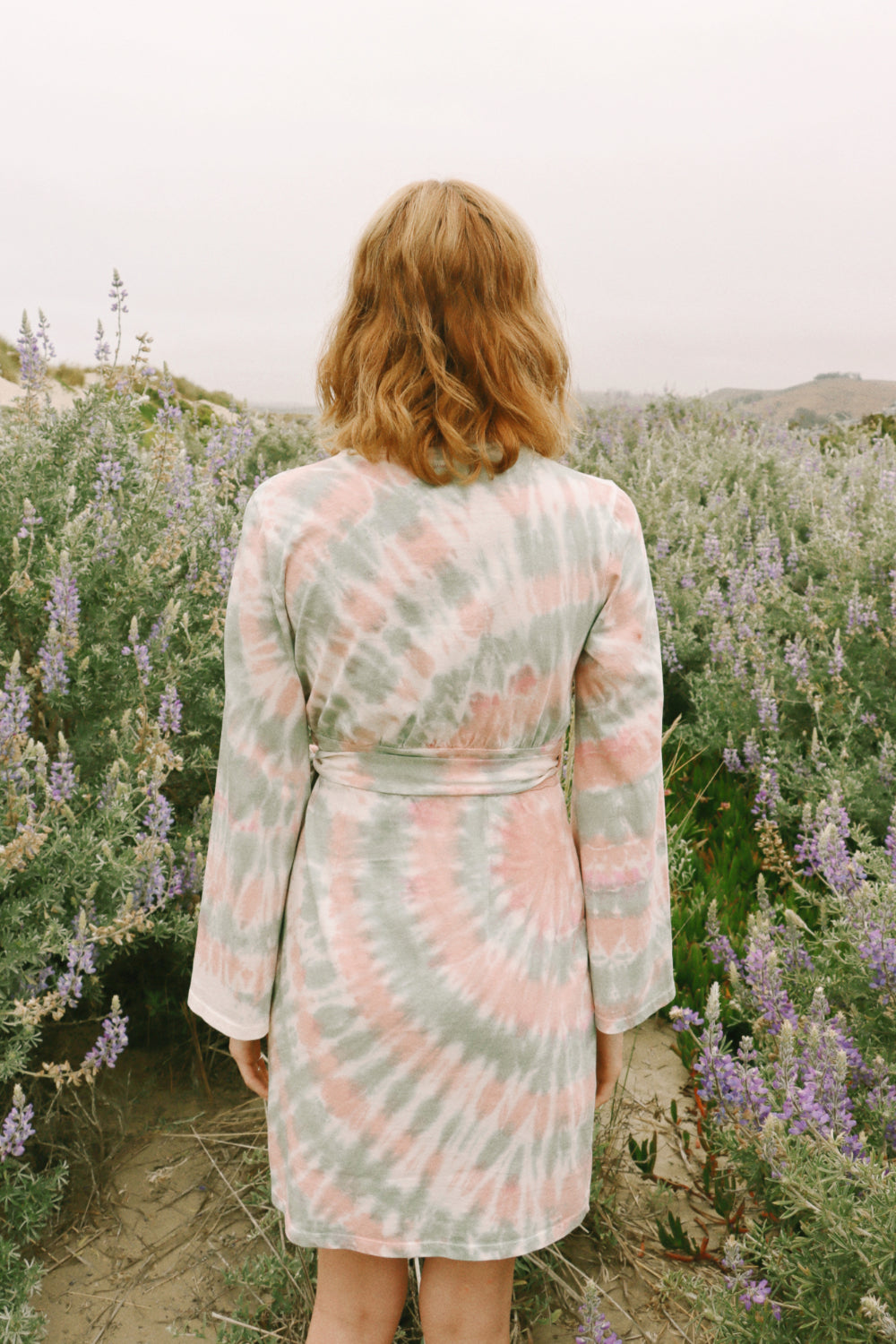 A stylish Sunrise Dress Tie-Dye featuring a saddle pink tie-dye pattern and wrap bell sleeves, perfect for any occasion.