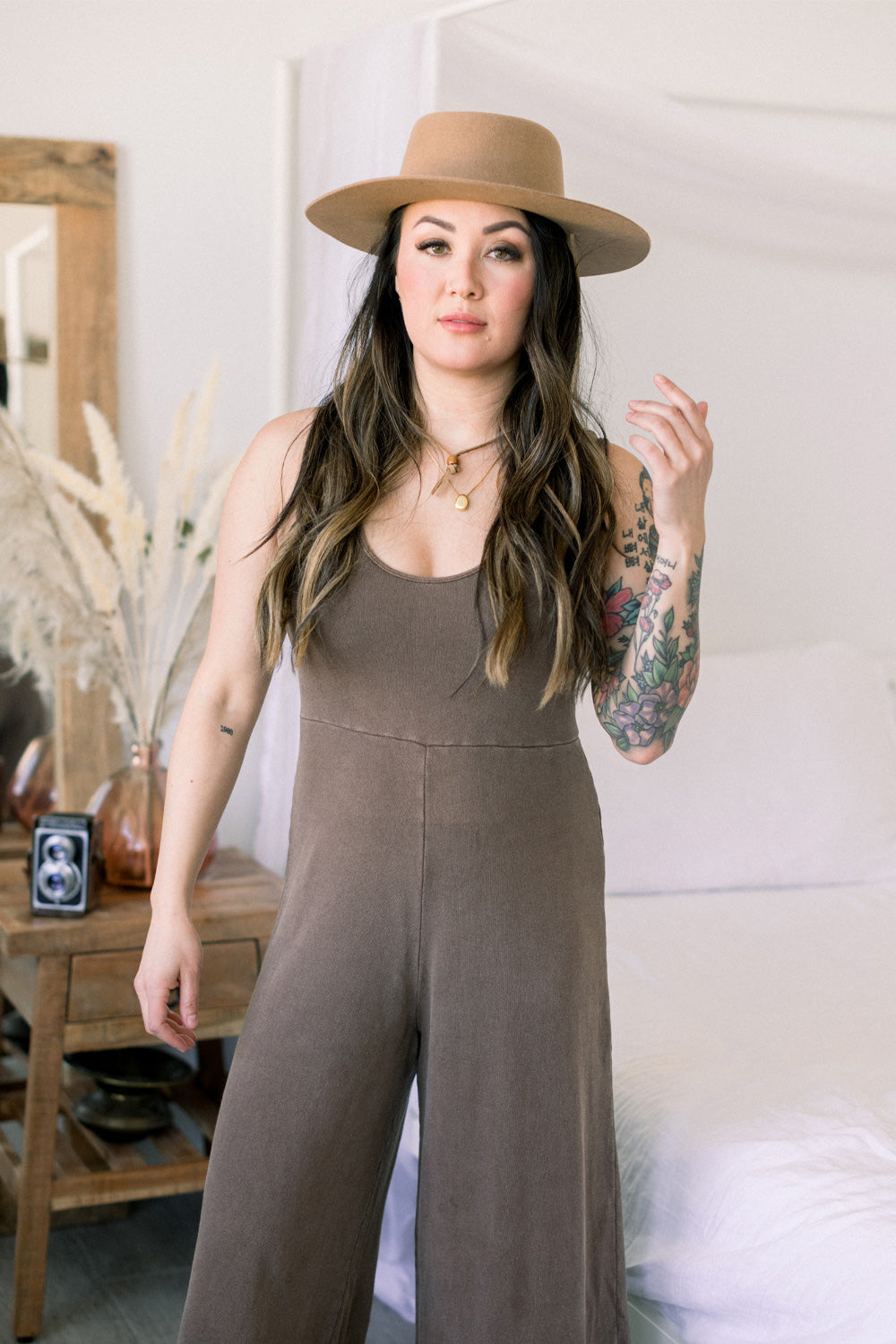 A stylish Sunset Jumpsuit featuring a waist-defining seam, wide legs, and v-neck detailing, available in Washed Black, Sand, and Persimmon colors.