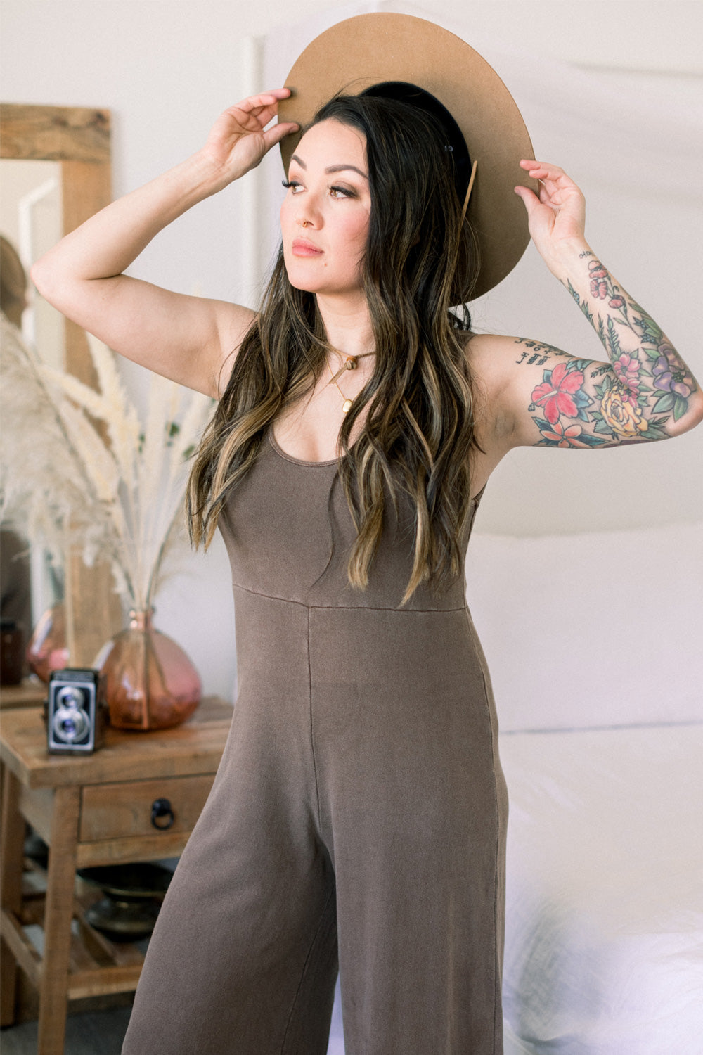 A stylish Sunset Jumpsuit featuring a waist-defining seam, wide legs, and v-neck detailing, available in Washed Black, Sand, and Persimmon colors.