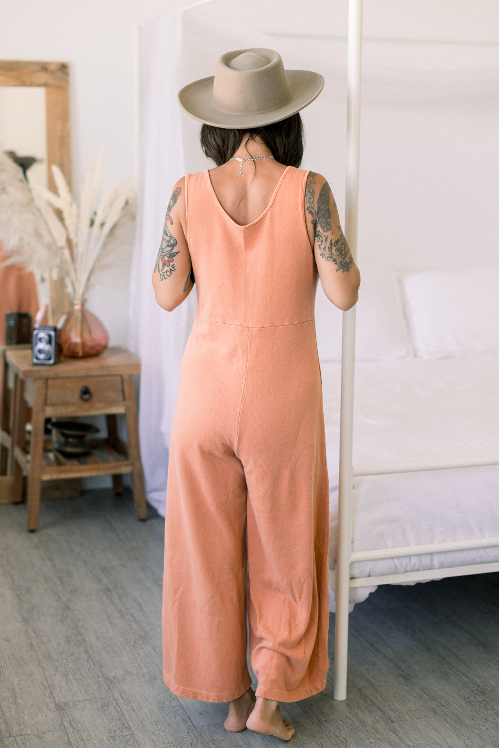 A stylish Sunset Jumpsuit featuring a waist-defining seam, wide legs, and v-neck detailing, available in Washed Black, Sand, and Persimmon colors.