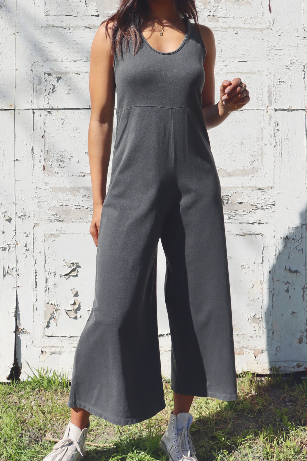 A stylish Sunset Jumpsuit featuring a waist-defining seam, wide legs, and v-neck detailing, available in Washed Black, Sand, and Persimmon colors.