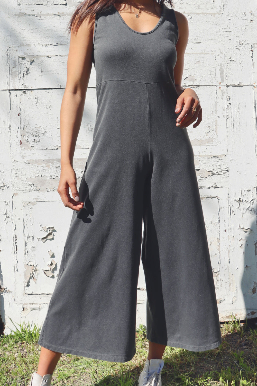 A stylish Sunset Jumpsuit featuring a waist-defining seam, wide legs, and v-neck detailing, available in Washed Black, Sand, and Persimmon colors.