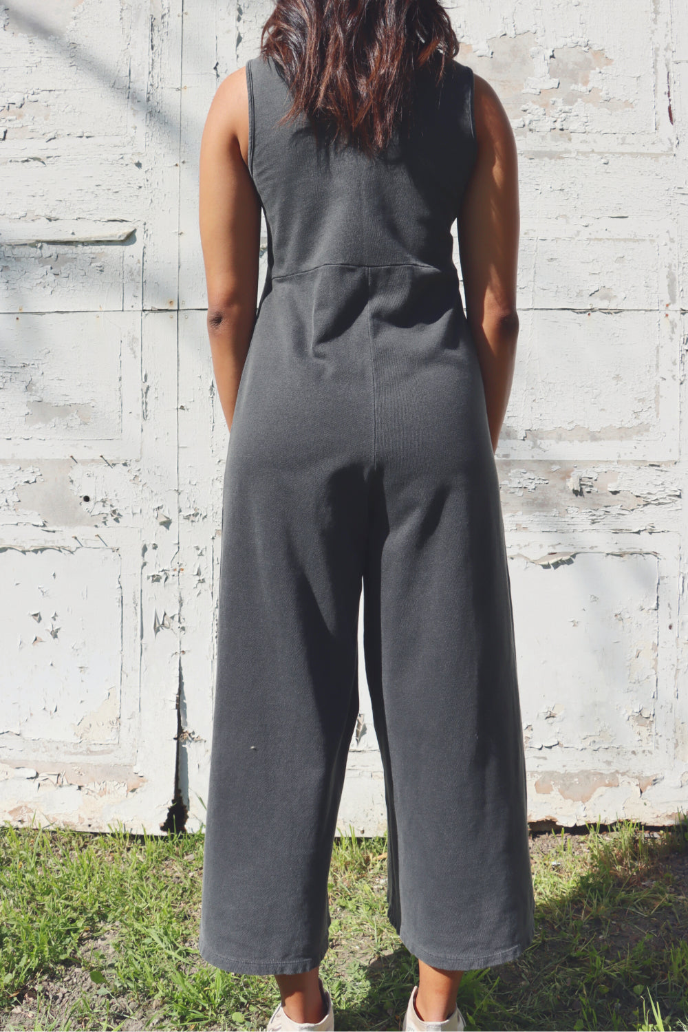 A stylish Sunset Jumpsuit featuring a waist-defining seam, wide legs, and v-neck detailing, available in Washed Black, Sand, and Persimmon colors.